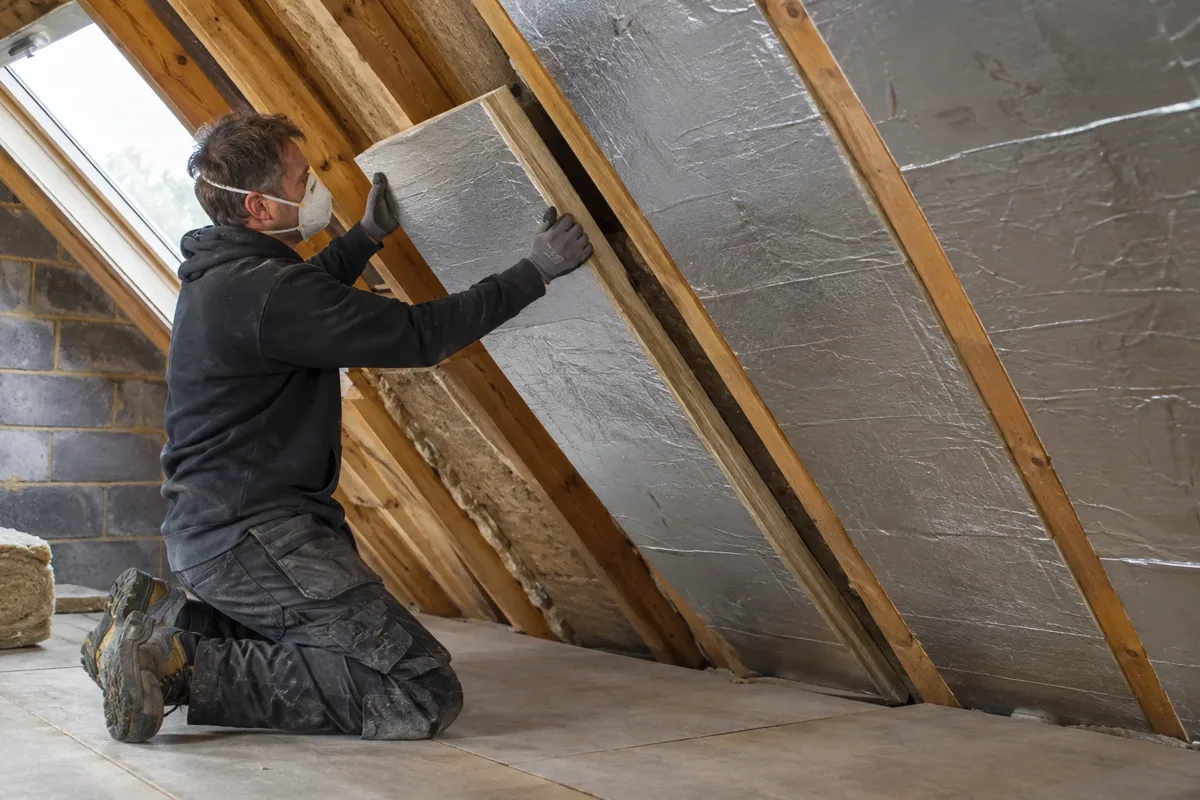 Installer fitting rigid insulation boards between timber roof rafters