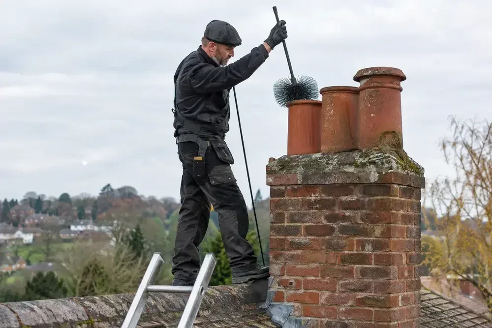 Chimney worker brushing a chimney pot from roof level